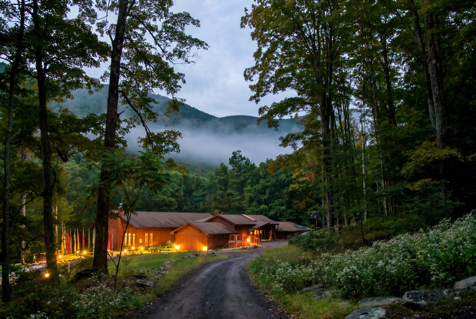 Menla Mountain Retreat at dusk, lights glowing beneath a misty Catskill valley